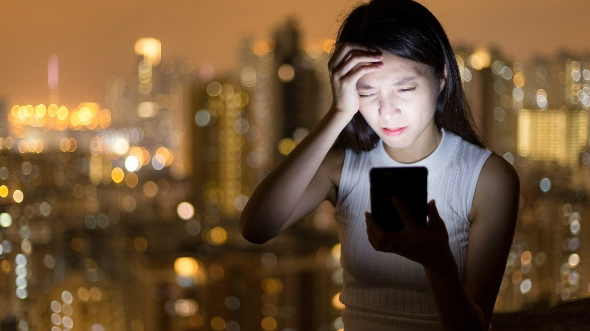 une femme ayant mal à la tête en travaillant avec son téléphone.