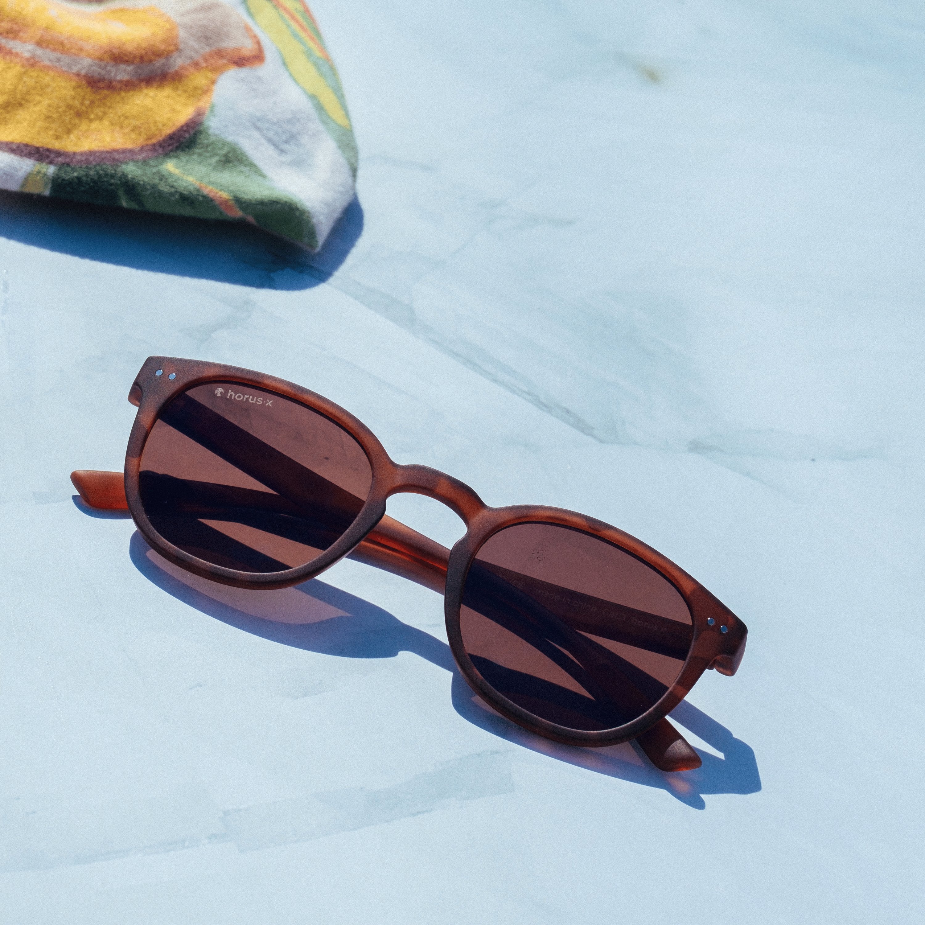 Lunettes Stockholm Sun posées sur une table en marbre avec un bandana vert et jaune