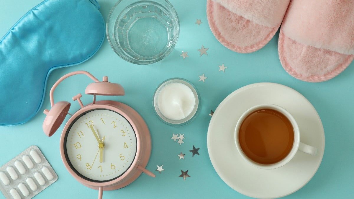 une horloge, une paire de dormeuses, une tasse de thé, un verre d'eau et un masque de sommeil sur la table.