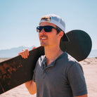 Notre cofondateur Paul avec les One Sun de profil avec une sandboard sur l'épaule dans le désert