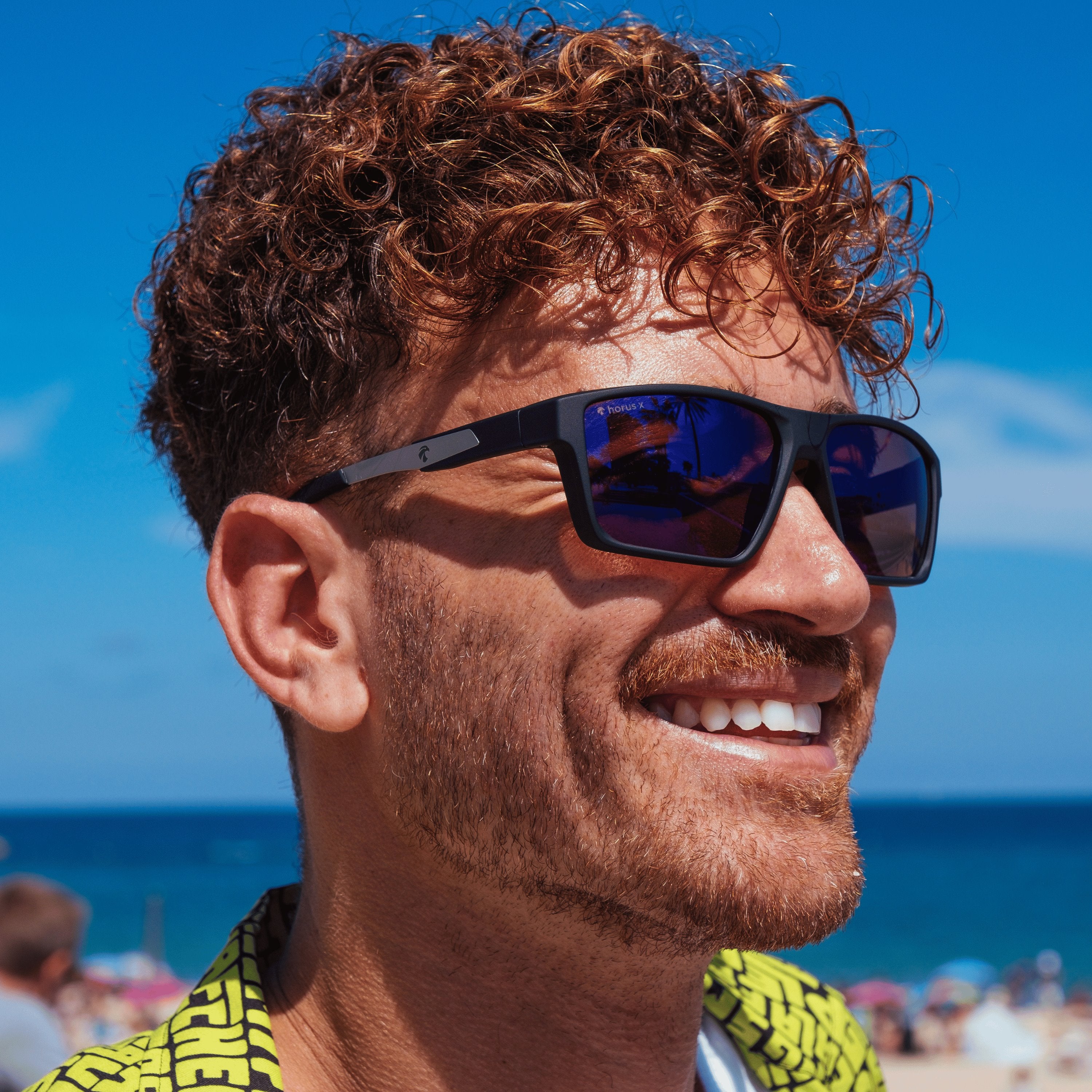 Portrait de Lucas devant l'océan et le ciel bleue équipé des lunettes de soleil One Revo Sun